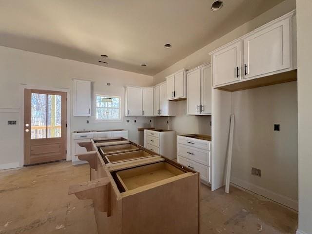 kitchen featuring unfinished concrete flooring, white cabinets, a kitchen island, and baseboards