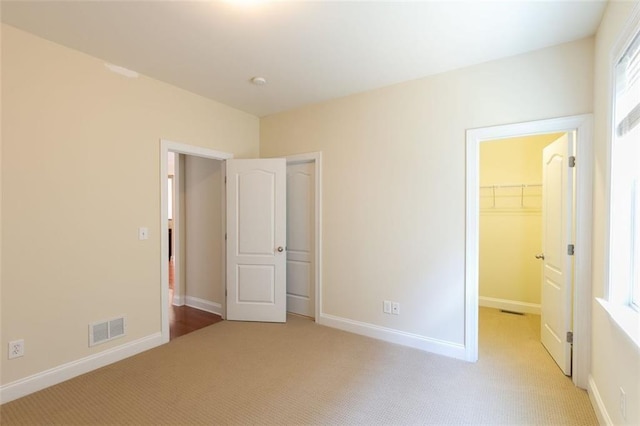 unfurnished bedroom with light colored carpet, a spacious closet, and a closet