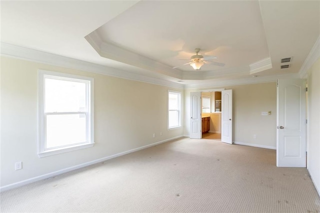 unfurnished bedroom with light carpet, a tray ceiling, crown molding, and ensuite bathroom