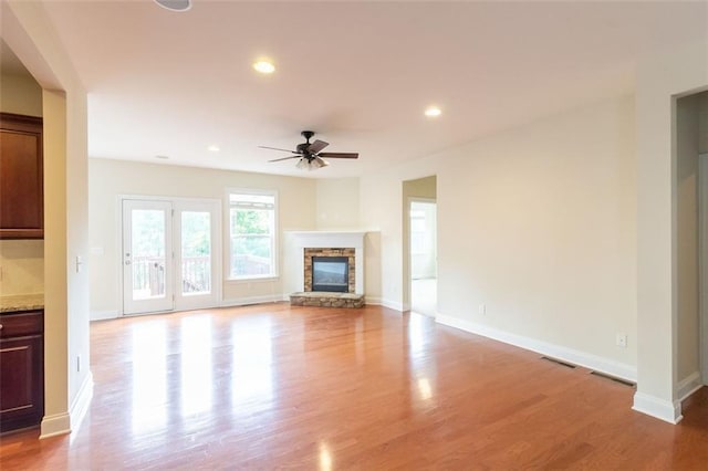 unfurnished living room with a stone fireplace, light hardwood / wood-style flooring, and ceiling fan