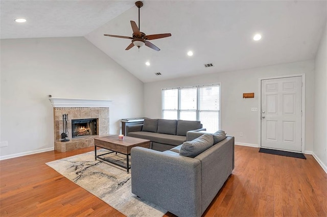 living area featuring baseboards, visible vents, wood finished floors, vaulted ceiling, and a stone fireplace