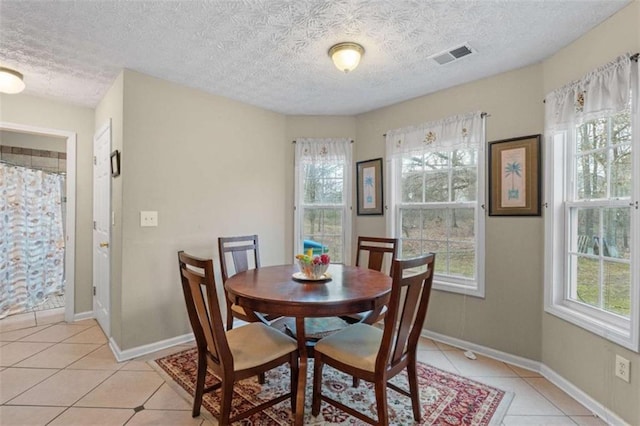 dining space featuring light tile patterned floors, baseboards, visible vents, and a textured ceiling