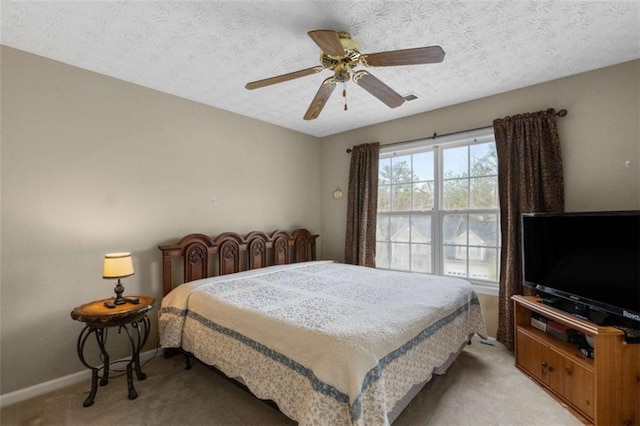 bedroom featuring visible vents, baseboards, a ceiling fan, light colored carpet, and a textured ceiling