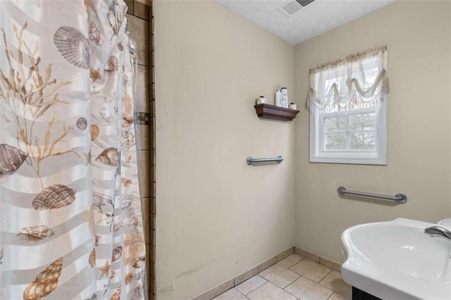 bathroom featuring a textured ceiling, tile patterned flooring, a sink, visible vents, and baseboards