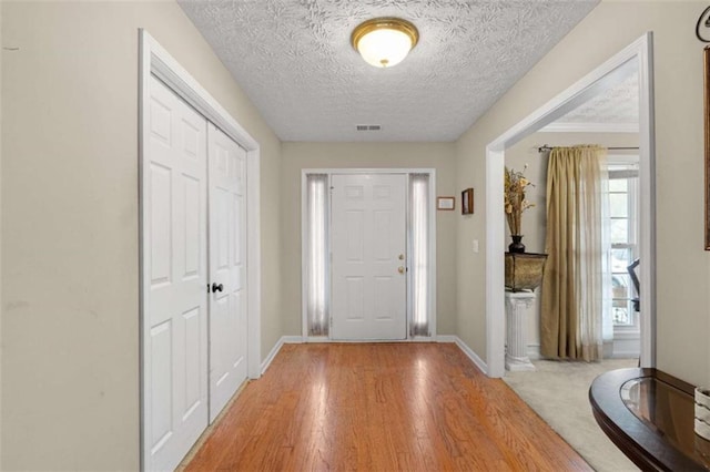 entrance foyer featuring a textured ceiling, light wood finished floors, visible vents, and baseboards