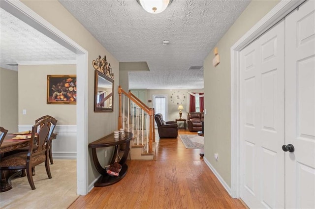 corridor featuring a textured ceiling, a wainscoted wall, visible vents, stairway, and light wood finished floors