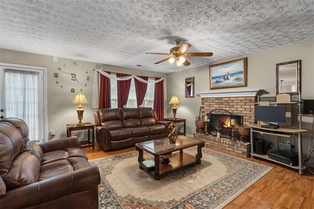 living area featuring a brick fireplace, ceiling fan, a textured ceiling, and wood finished floors