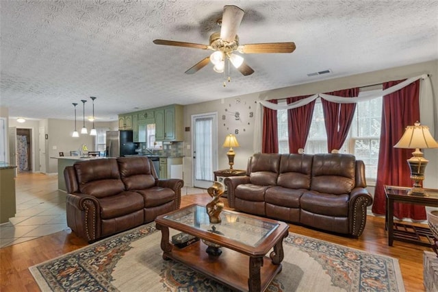 living area with light wood-type flooring, ceiling fan, visible vents, and a textured ceiling