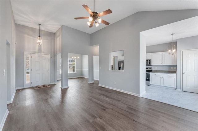 unfurnished living room featuring decorative columns, dark hardwood / wood-style floors, ceiling fan with notable chandelier, and high vaulted ceiling