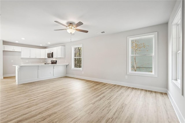 unfurnished living room featuring visible vents, light wood finished floors, a ceiling fan, and baseboards