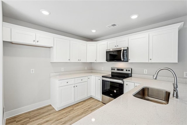 kitchen with light stone counters, light wood finished floors, stainless steel appliances, visible vents, and a sink