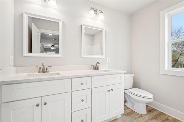 bathroom with double vanity, a sink, toilet, and wood finished floors