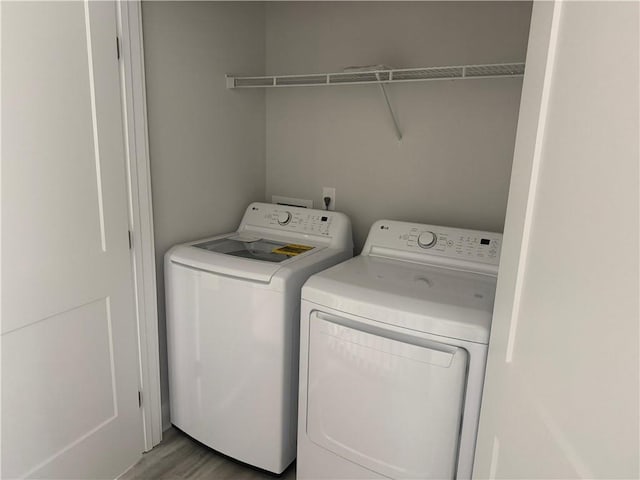 clothes washing area with laundry area, washing machine and clothes dryer, and wood finished floors