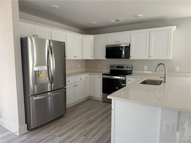 kitchen with visible vents, light stone counters, a peninsula, stainless steel appliances, and a sink