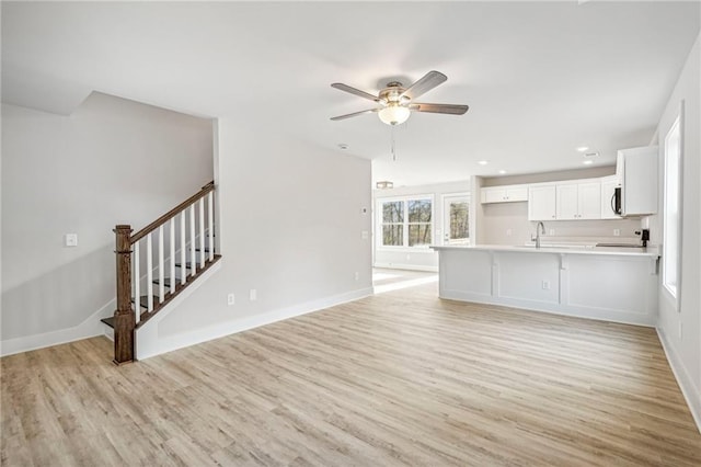 unfurnished living room with light wood-style floors, ceiling fan, stairway, and baseboards