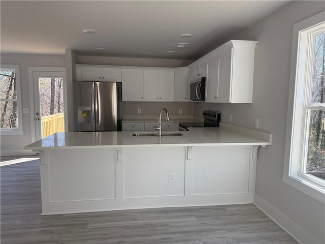 kitchen featuring light countertops, appliances with stainless steel finishes, white cabinets, a sink, and a peninsula