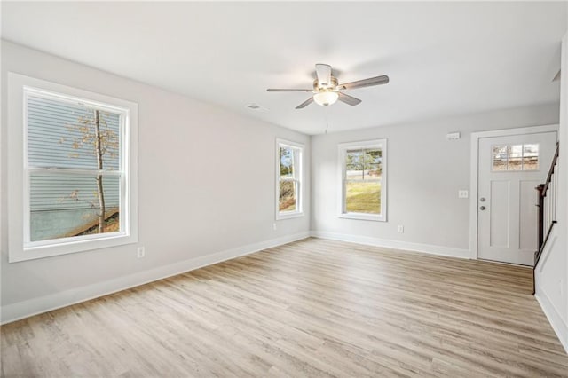 empty room with light wood finished floors, visible vents, baseboards, a ceiling fan, and stairs