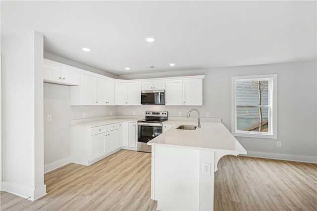 kitchen featuring light countertops, appliances with stainless steel finishes, light wood-style floors, a sink, and a peninsula