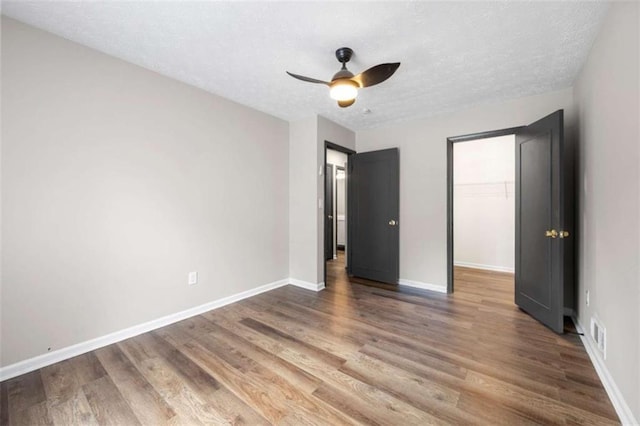 unfurnished bedroom featuring hardwood / wood-style floors, a walk in closet, ceiling fan, a textured ceiling, and a closet