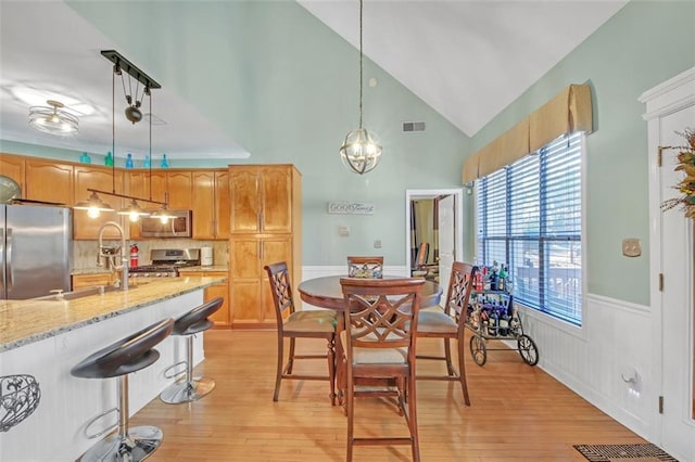 dining area with a wainscoted wall, vaulted ceiling, visible vents, and light wood finished floors