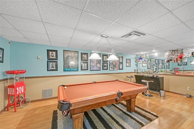 game room with a drop ceiling, wood finished floors, visible vents, and wet bar