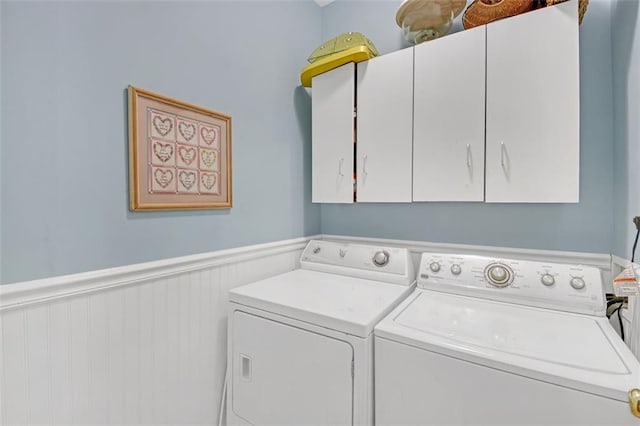 laundry room featuring a wainscoted wall, cabinet space, and washer and clothes dryer