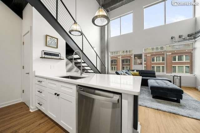 kitchen featuring sink, white cabinetry, stainless steel dishwasher, pendant lighting, and hardwood / wood-style floors