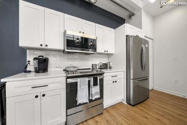 kitchen with white cabinetry, decorative backsplash, stainless steel appliances, and light wood-type flooring