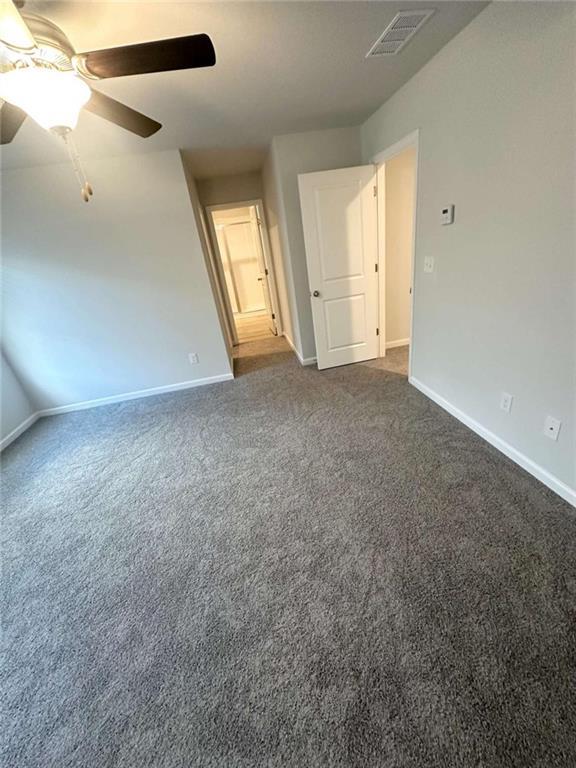 empty room featuring baseboards, visible vents, dark colored carpet, and ceiling fan