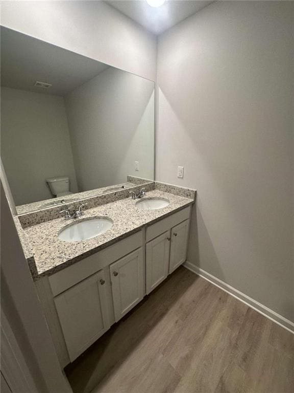 bathroom with double vanity, toilet, wood finished floors, and a sink