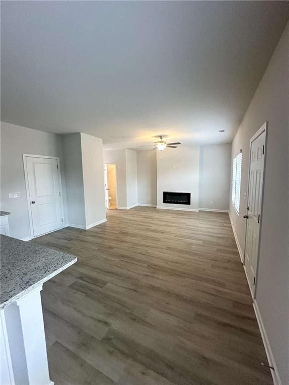 unfurnished living room with baseboards, a ceiling fan, a fireplace, and dark wood-style flooring