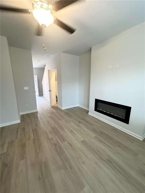 unfurnished living room featuring a glass covered fireplace, baseboards, a ceiling fan, and wood finished floors