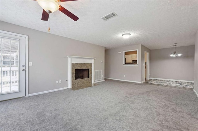 unfurnished living room with ceiling fan with notable chandelier, a textured ceiling, a fireplace, and carpet floors