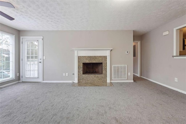 unfurnished living room featuring ceiling fan, a premium fireplace, carpet floors, and a textured ceiling