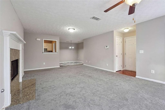 unfurnished living room featuring a textured ceiling, ceiling fan, a fireplace, and dark colored carpet