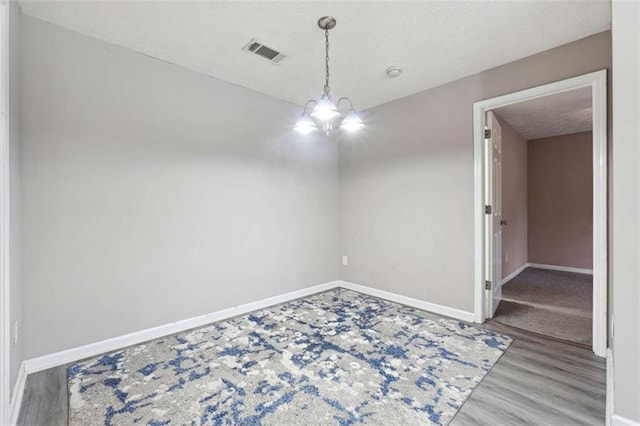 spare room with a textured ceiling, an inviting chandelier, and hardwood / wood-style flooring