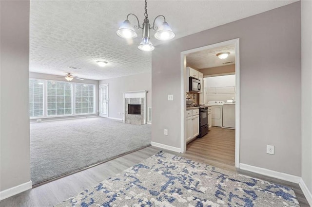 living room with ceiling fan with notable chandelier, a textured ceiling, washing machine and dryer, and light hardwood / wood-style floors