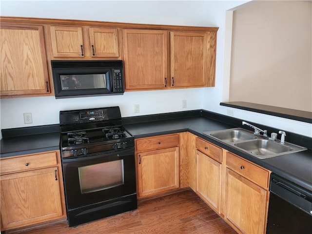 kitchen featuring black appliances, wood finished floors, dark countertops, and a sink