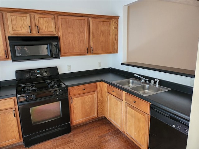 kitchen featuring dark countertops, black appliances, a sink, and wood finished floors