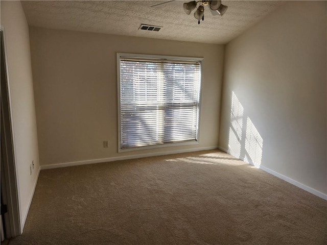 carpeted spare room featuring a textured ceiling, ceiling fan, visible vents, and baseboards