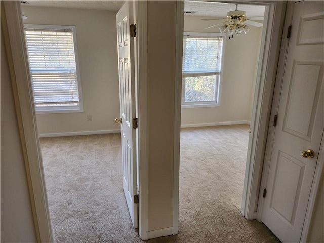 hall with baseboards and light colored carpet