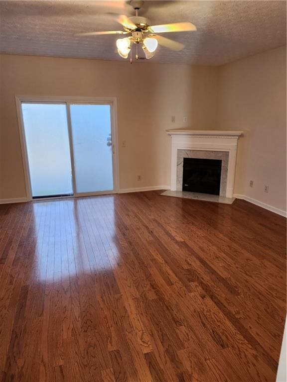 unfurnished living room with a textured ceiling, ceiling fan, a fireplace, baseboards, and dark wood finished floors