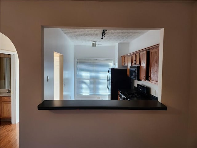 kitchen with a textured ceiling, a peninsula, a sink, black appliances, and dark countertops