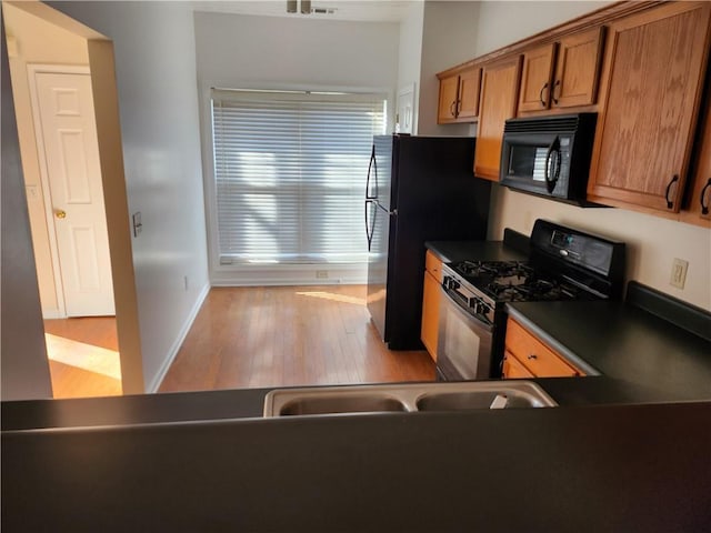 kitchen featuring dark countertops, black appliances, light wood-style flooring, and brown cabinets