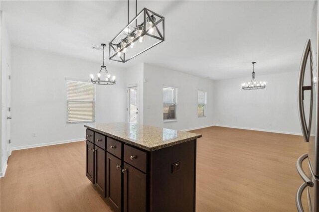 kitchen featuring pendant lighting, light hardwood / wood-style floors, a kitchen island, and light stone counters