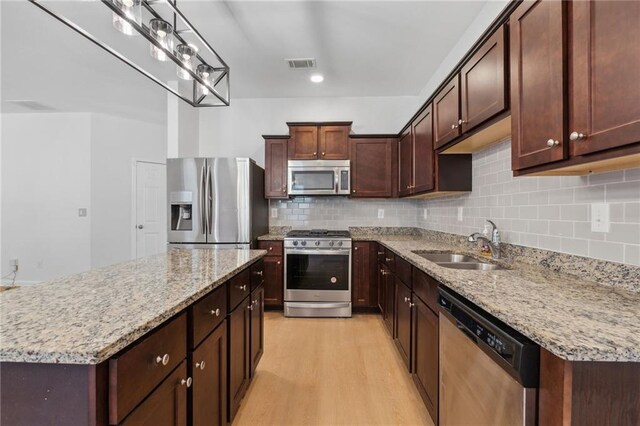 kitchen with light stone countertops, appliances with stainless steel finishes, light wood-type flooring, sink, and a kitchen island