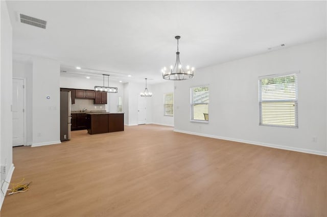 unfurnished living room featuring light wood-type flooring and an inviting chandelier