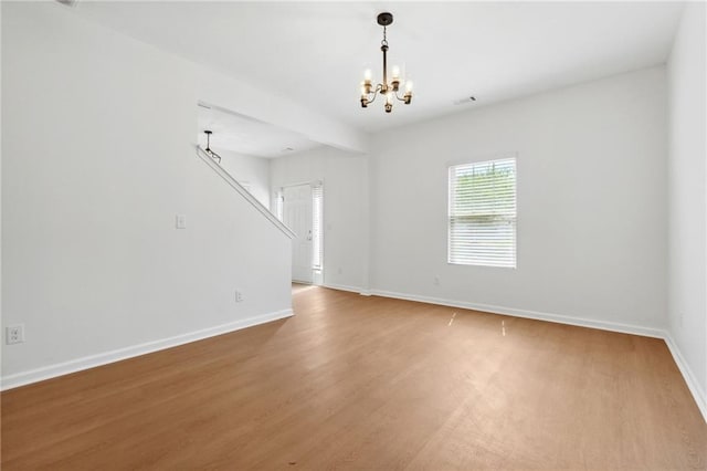 empty room with hardwood / wood-style floors and an inviting chandelier