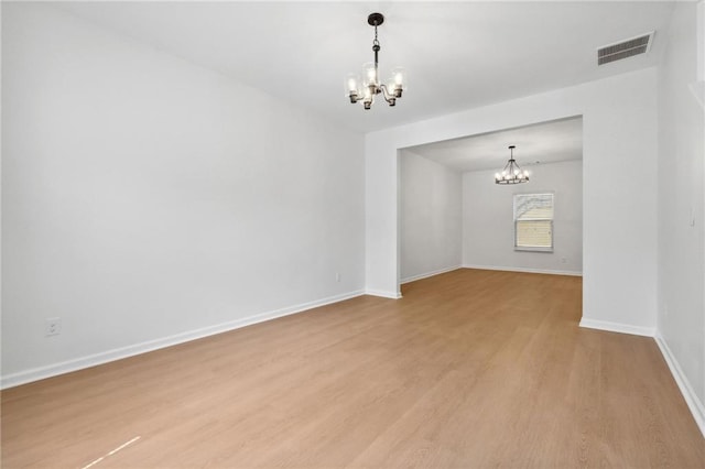 empty room with light hardwood / wood-style floors and an inviting chandelier