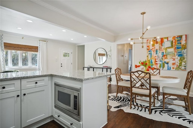 kitchen featuring light stone counters, dark wood-type flooring, crown molding, decorative light fixtures, and stainless steel microwave